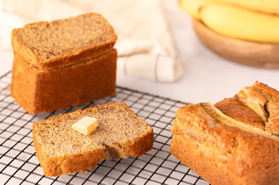 A loaf and two cut slices cooling on a wire rack
